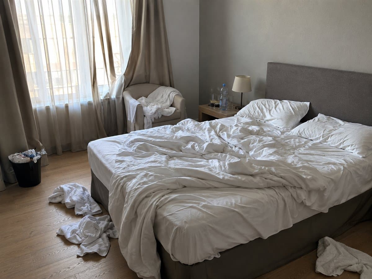 Chambre de meublé après un départ : lit défait, serviettes au sol, chevet encombré