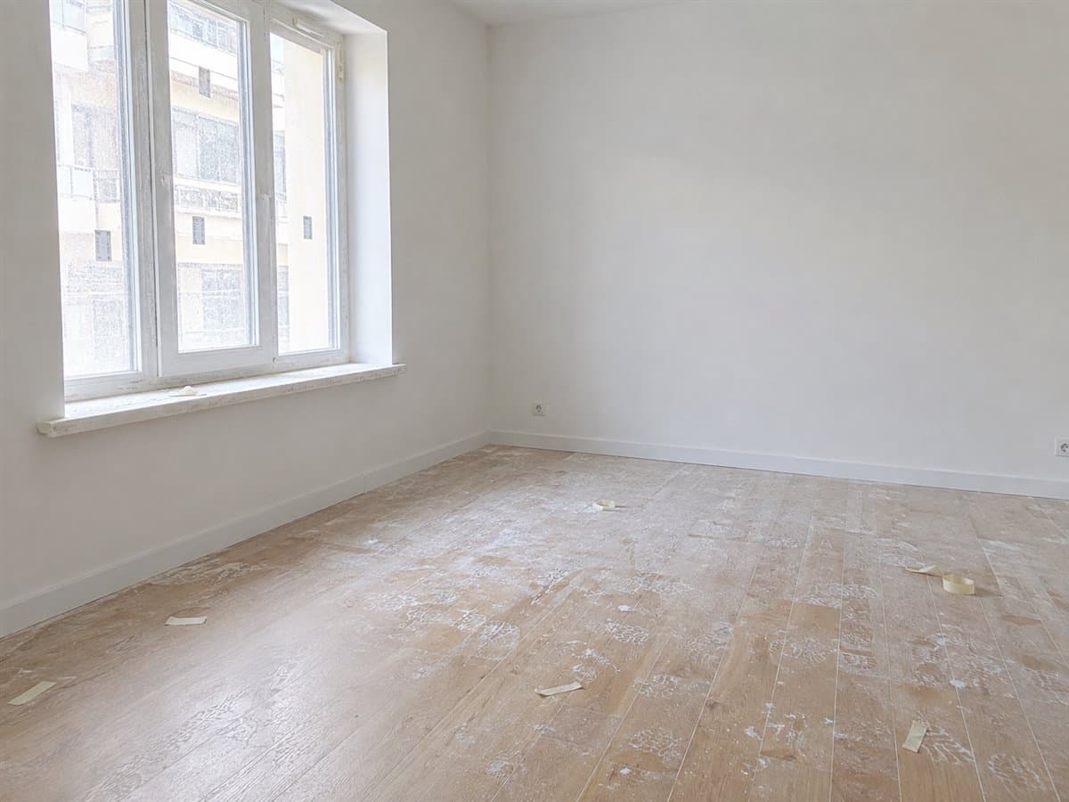 Pièce rénovée sous la poussière de chantier : parquet voilé de plâtre, résidus au sol